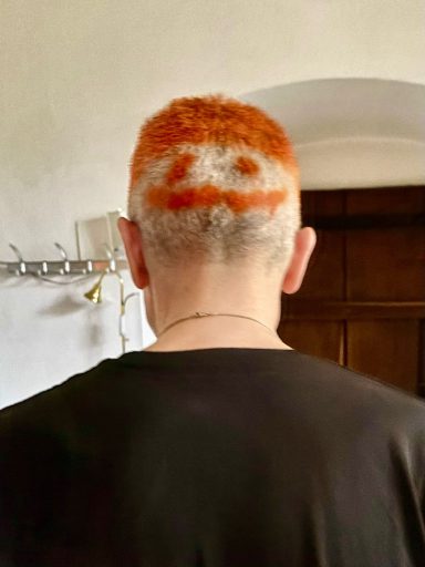 Mann mit rasiertem Haar, orangefarbener Frisur und lächelndem Gesichtsmuster im Nacken.